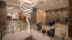 A modern lobby with a spiral light fixture, marble flooring, and blue seating areas. - Radisson Blu Pune Hinjawadi (Paud)