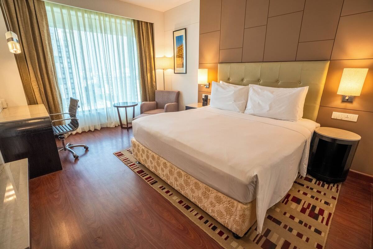 Una habitación de hotel con una cama grande, un escritorio, una silla, una mesita y vistas a un edificio desde la ventana.
