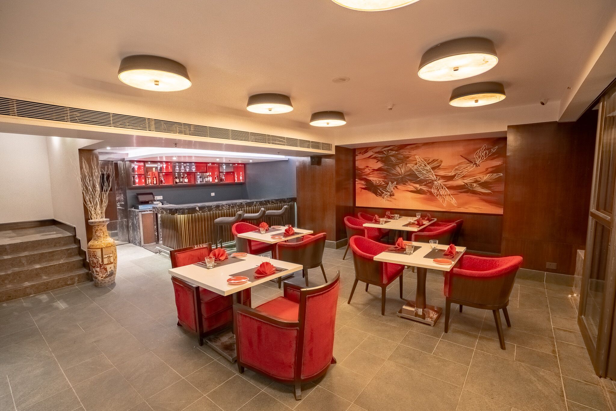 Un restaurante con sillas tapizadas en rojo, mesas blancas y un cuadro grande con motivos florales en la pared.