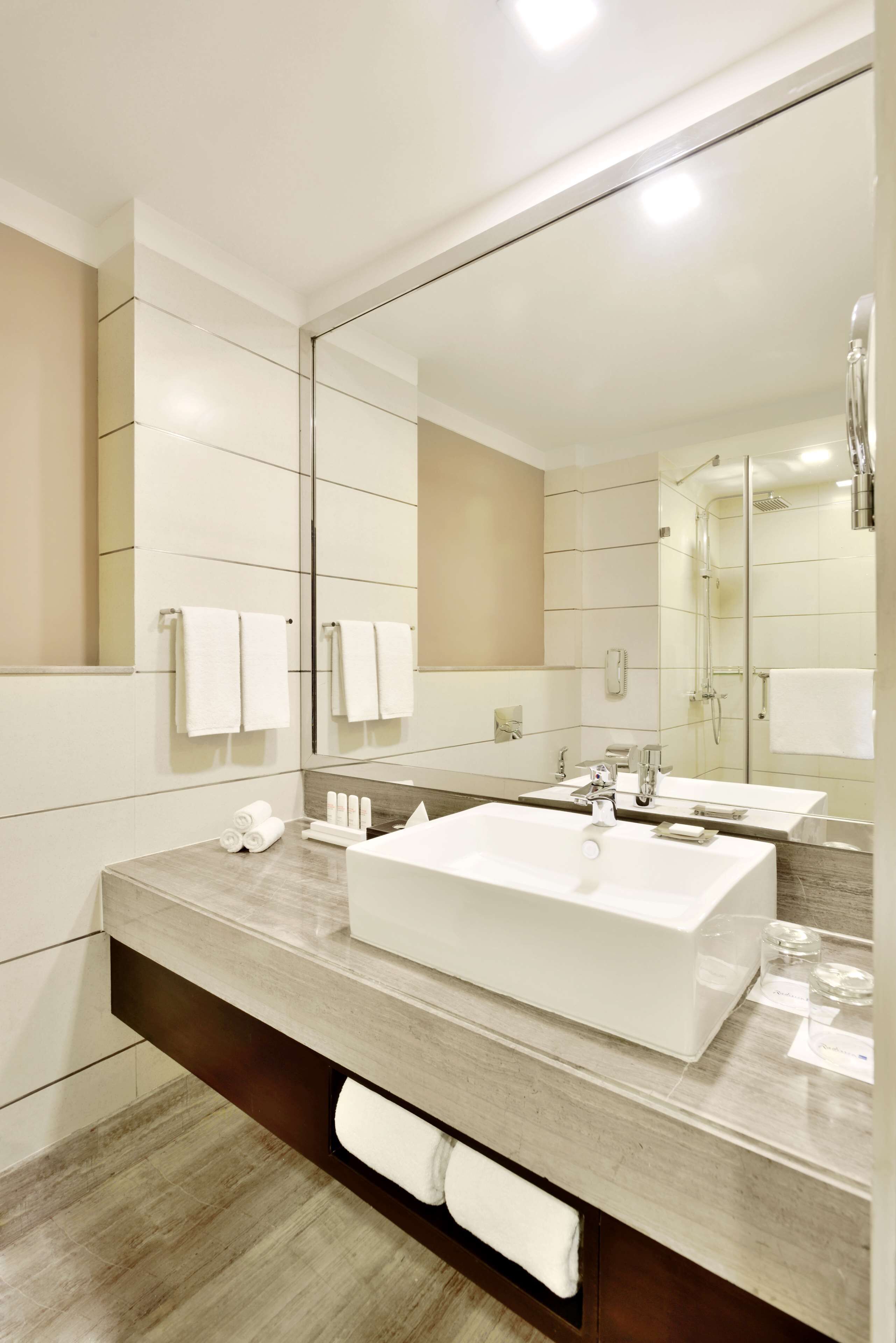 A modern bathroom with a large mirror, two sinks, and a shower.