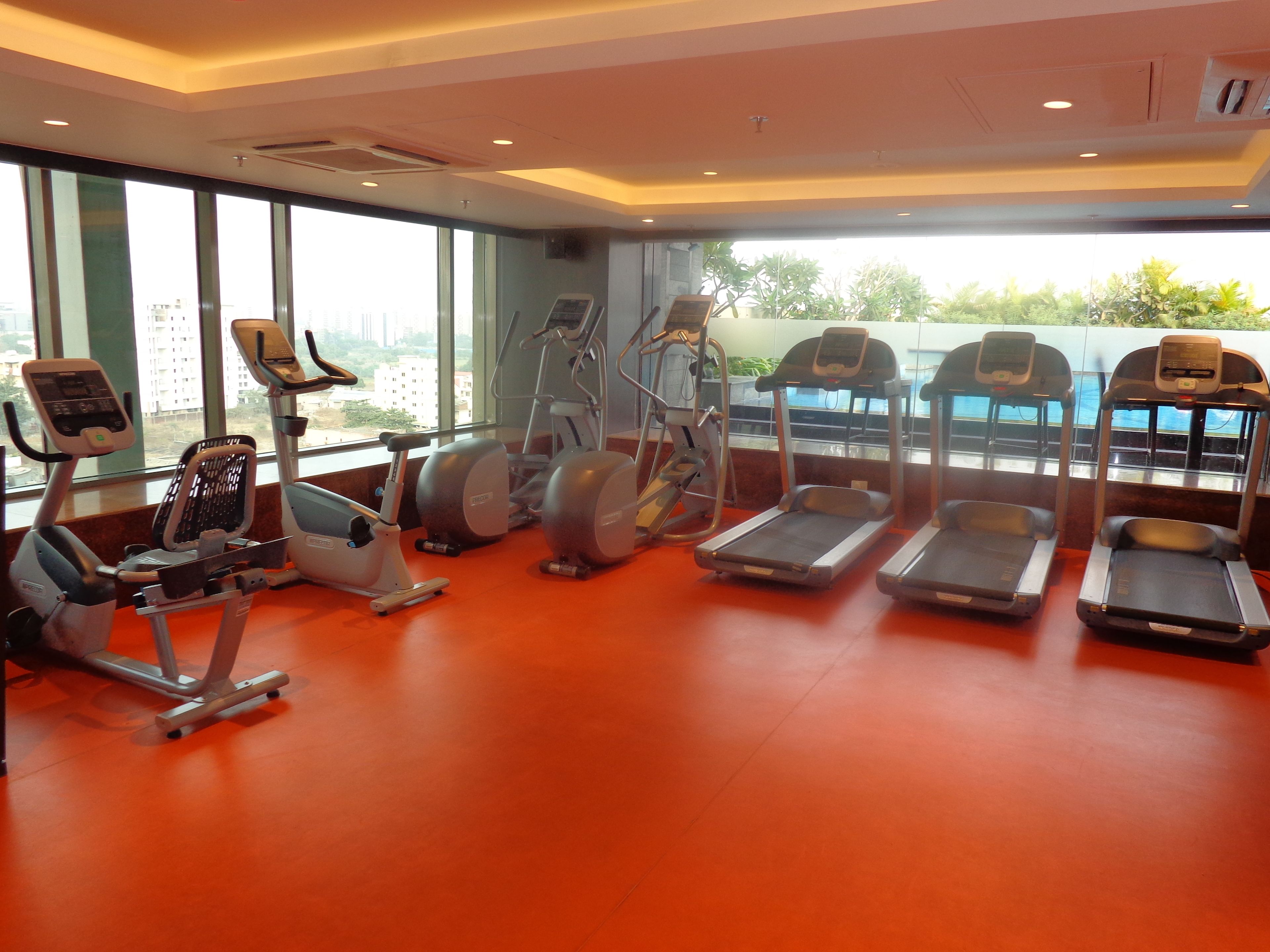 A gym with various cardio machines, large windows, and a view of buildings outside.