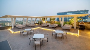 A rooftop patio with outdoor seating, a grill, and a view of the city skyline. - Radisson Blu Pune Hinjawadi (Paud)