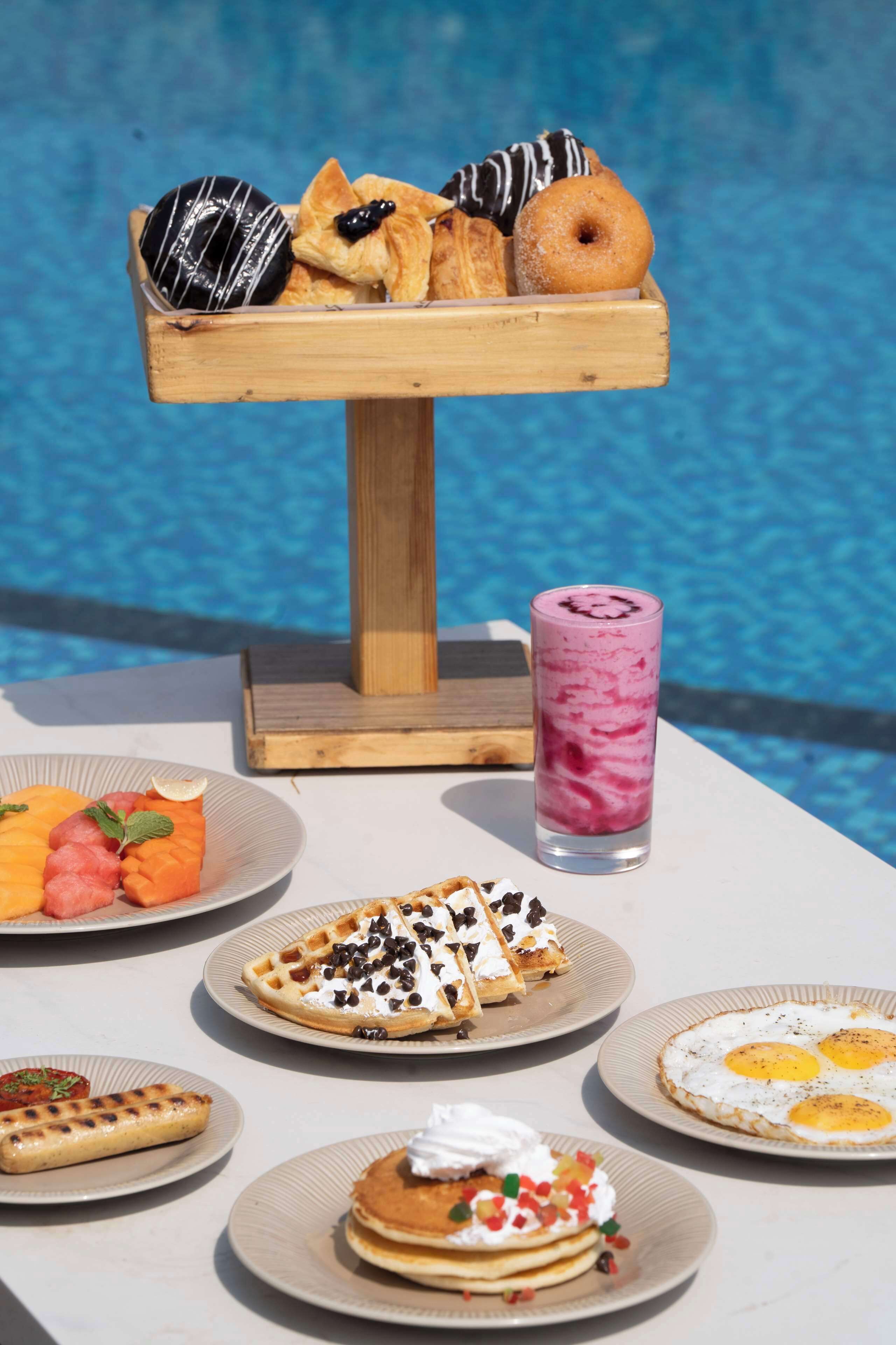 A breakfast buffet with various pastries, waffles, pancakes, and a smoothie.