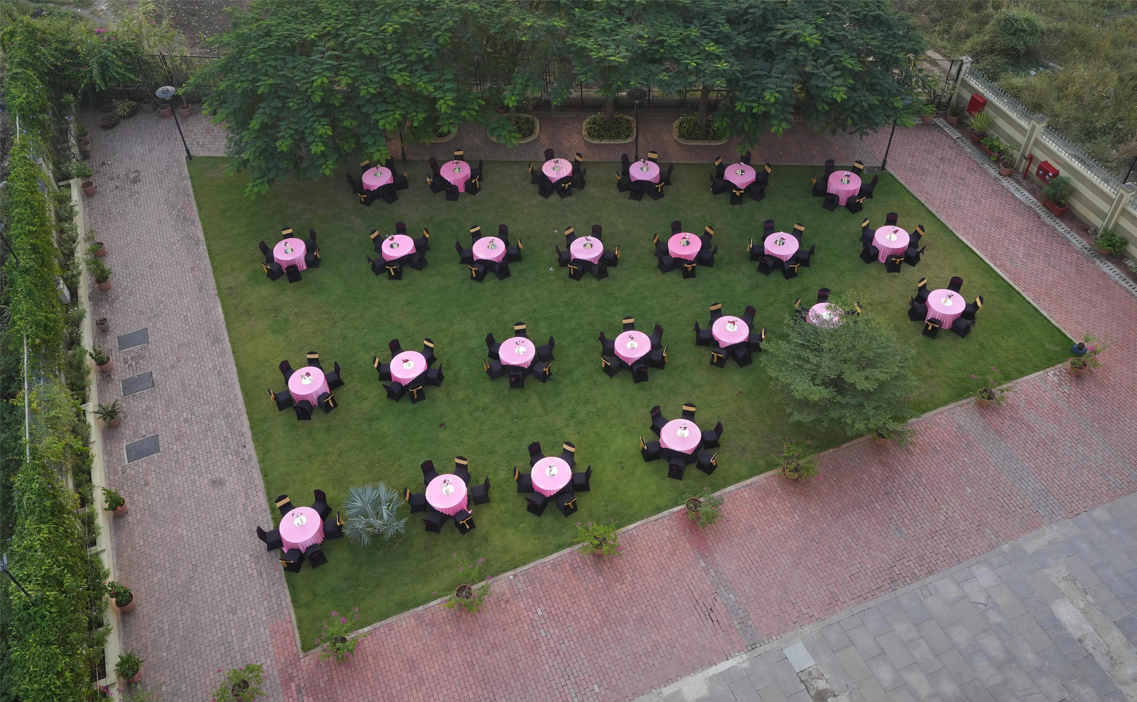 A rooftop garden with multiple round tables and chairs, surrounded by potted plants and trees.