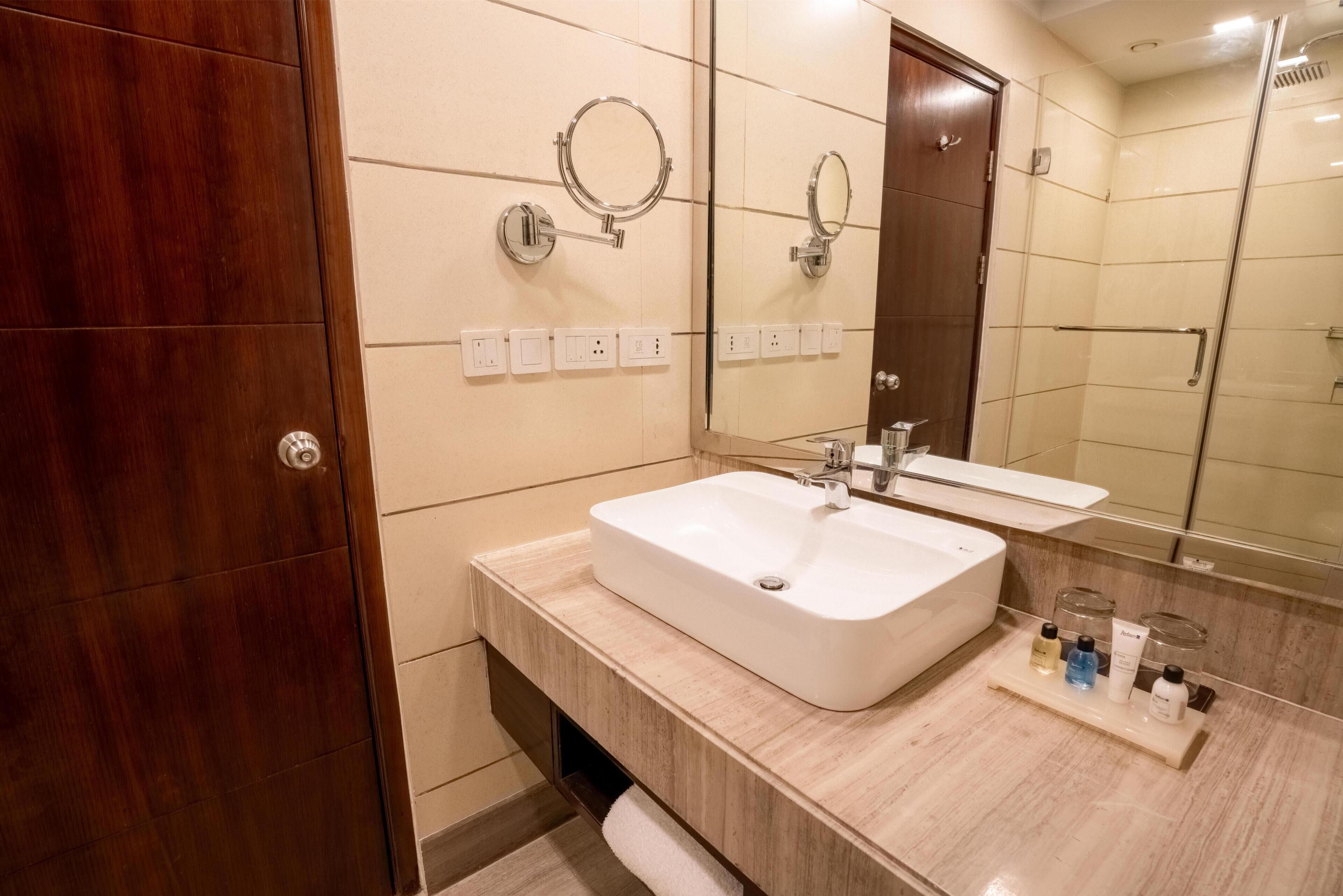 A bathroom with a white sink, a mirror, a towel rack, and a shower area.