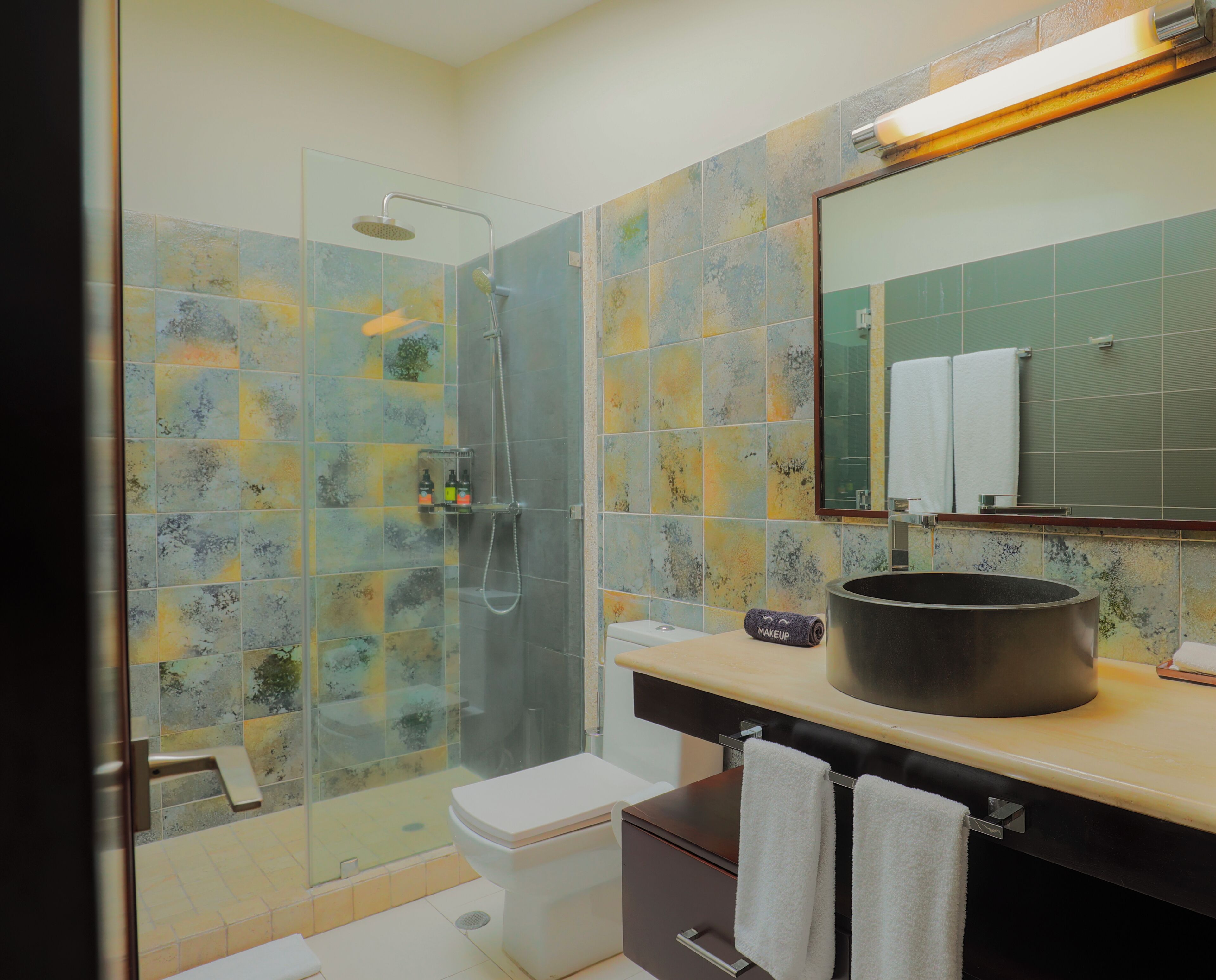Une salle de bain dotée d’une douche à parois de verre, de toilettes blanches, d’un meuble-lavabo avec un grand évier et d’un miroir au-dessus de l’évier.