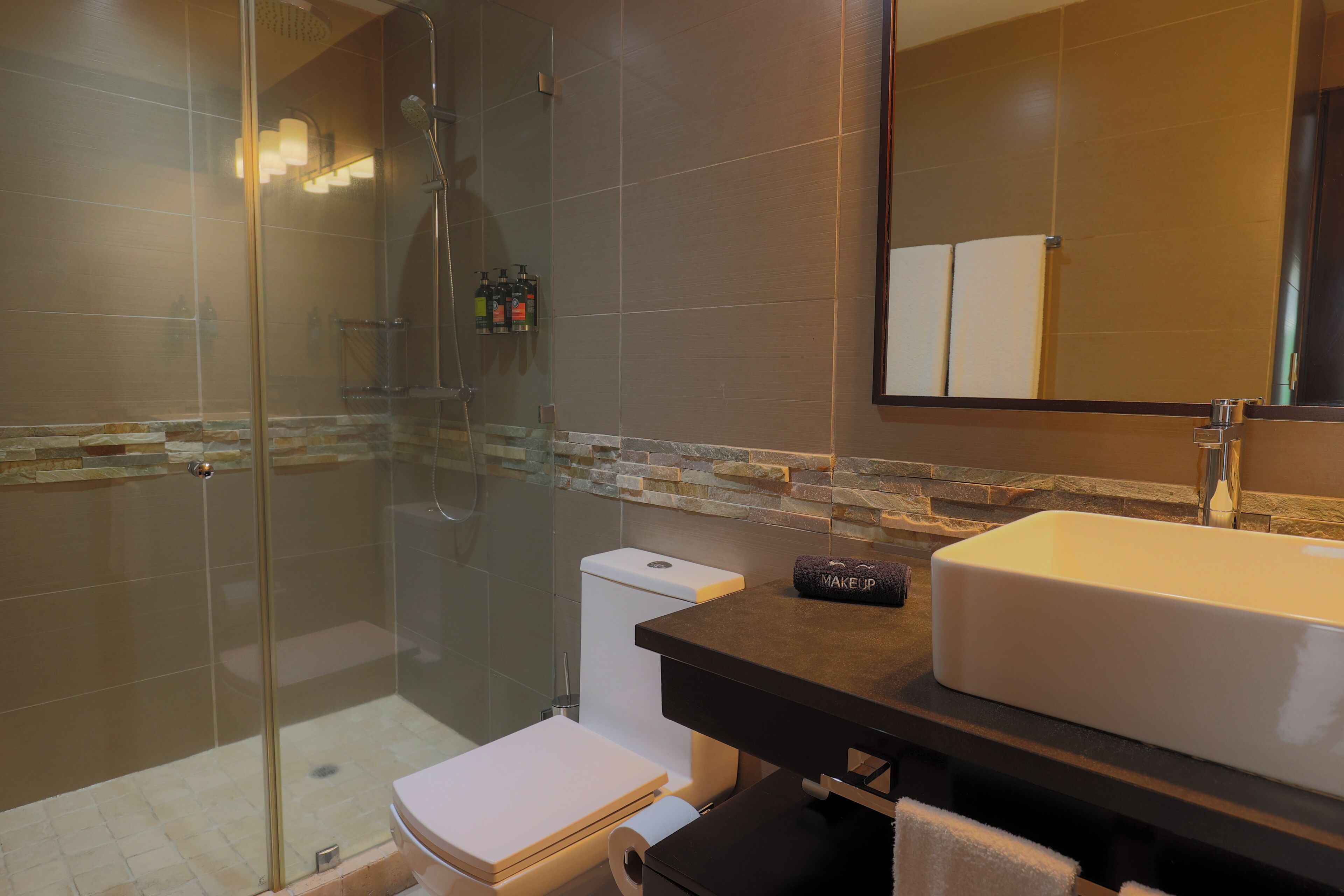 Un baño moderno con ducha envuelta en vidrio, inodoro y lavabo con espejo.
