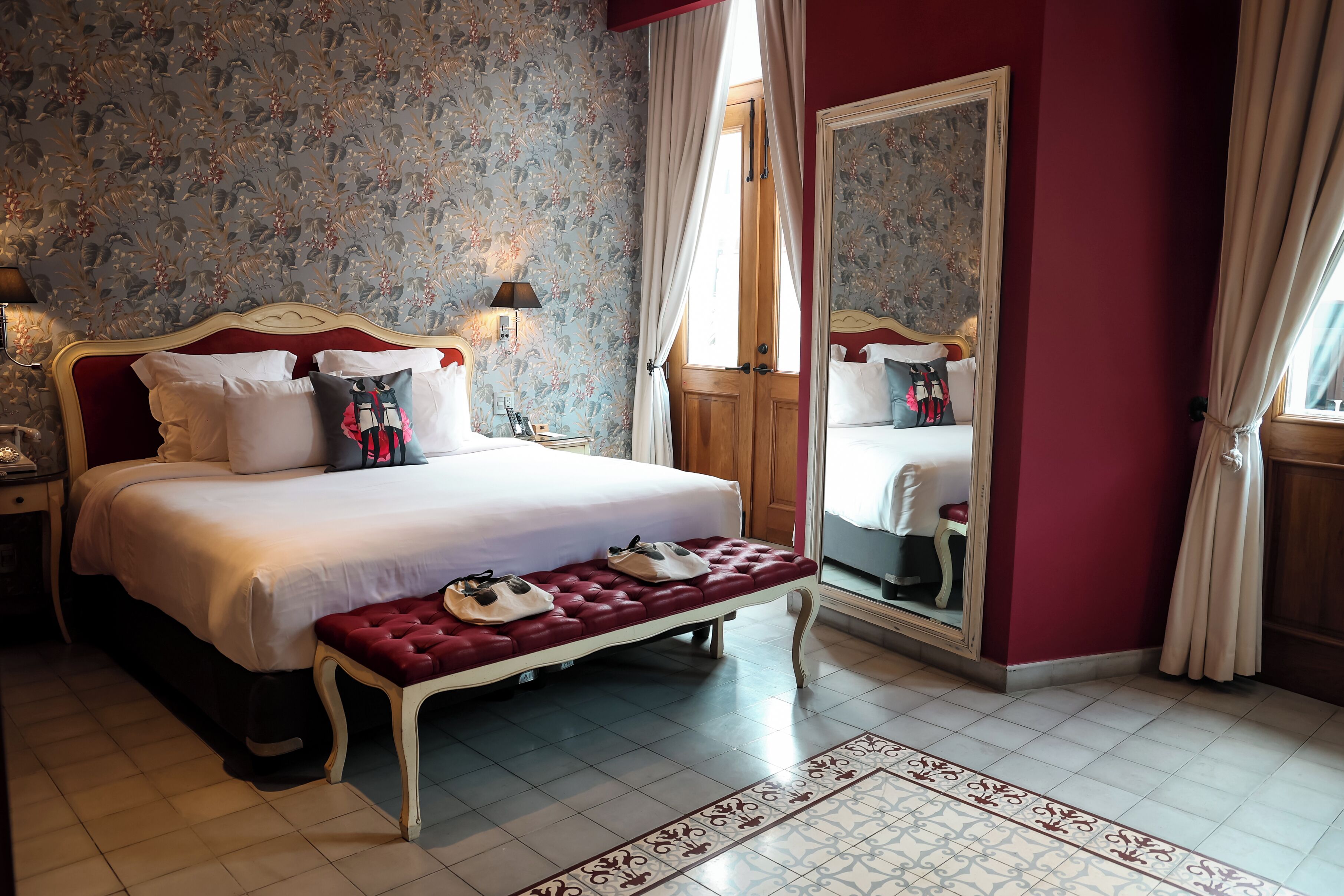 Une chambre à coucher avec un grand lit, un banc où sont posées des chaussures, un miroir et une table de chevet.