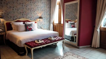 A bedroom with a large bed, a bench with shoes, a mirror, and a nightstand.
