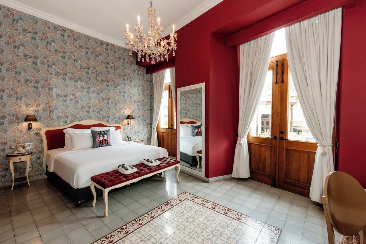 A bedroom with a large bed, a chandelier, a wooden door, and a mirror.