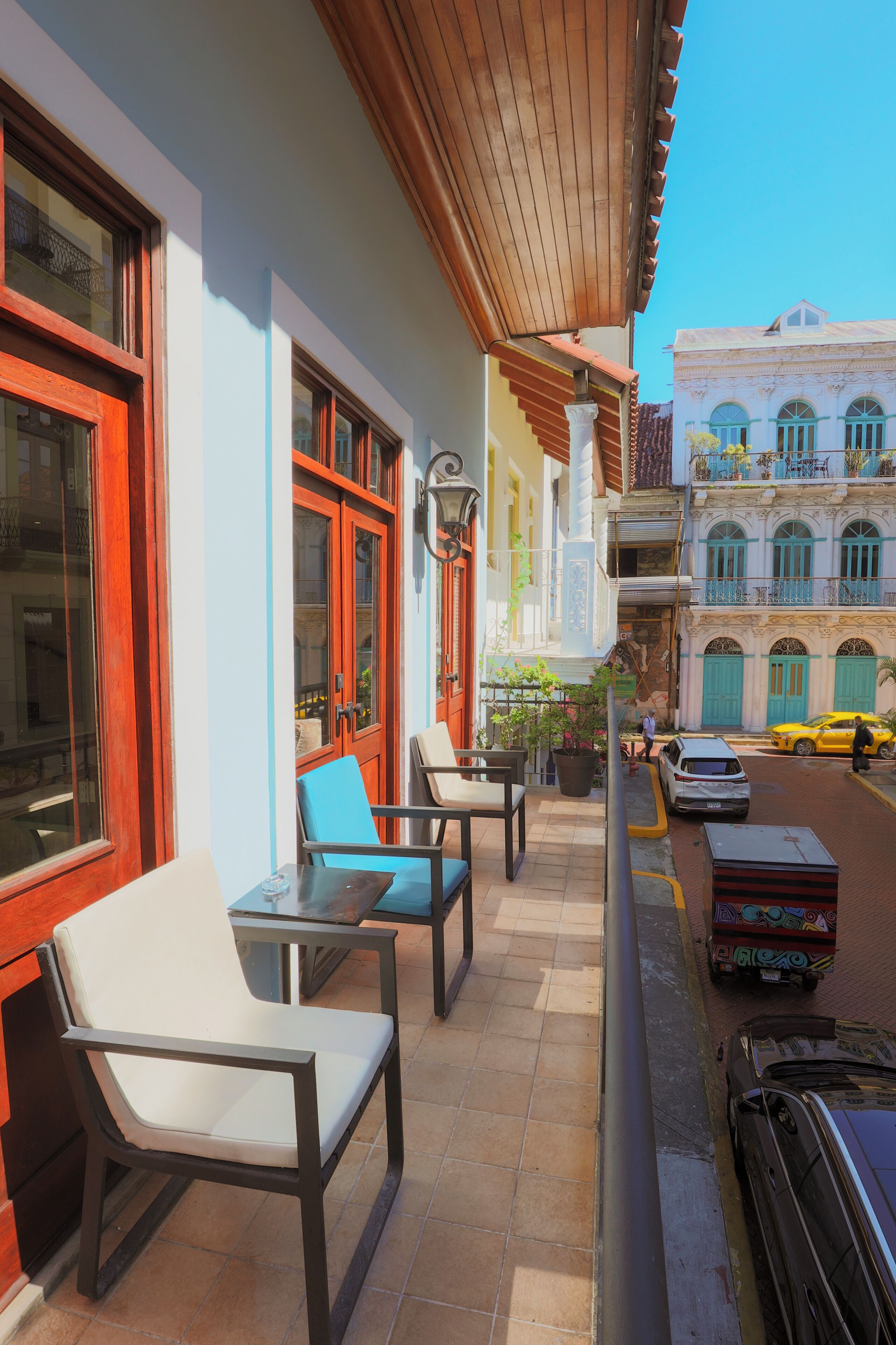 A balcony with outdoor seating, a car parked on the street, and a building with balconies in the background.