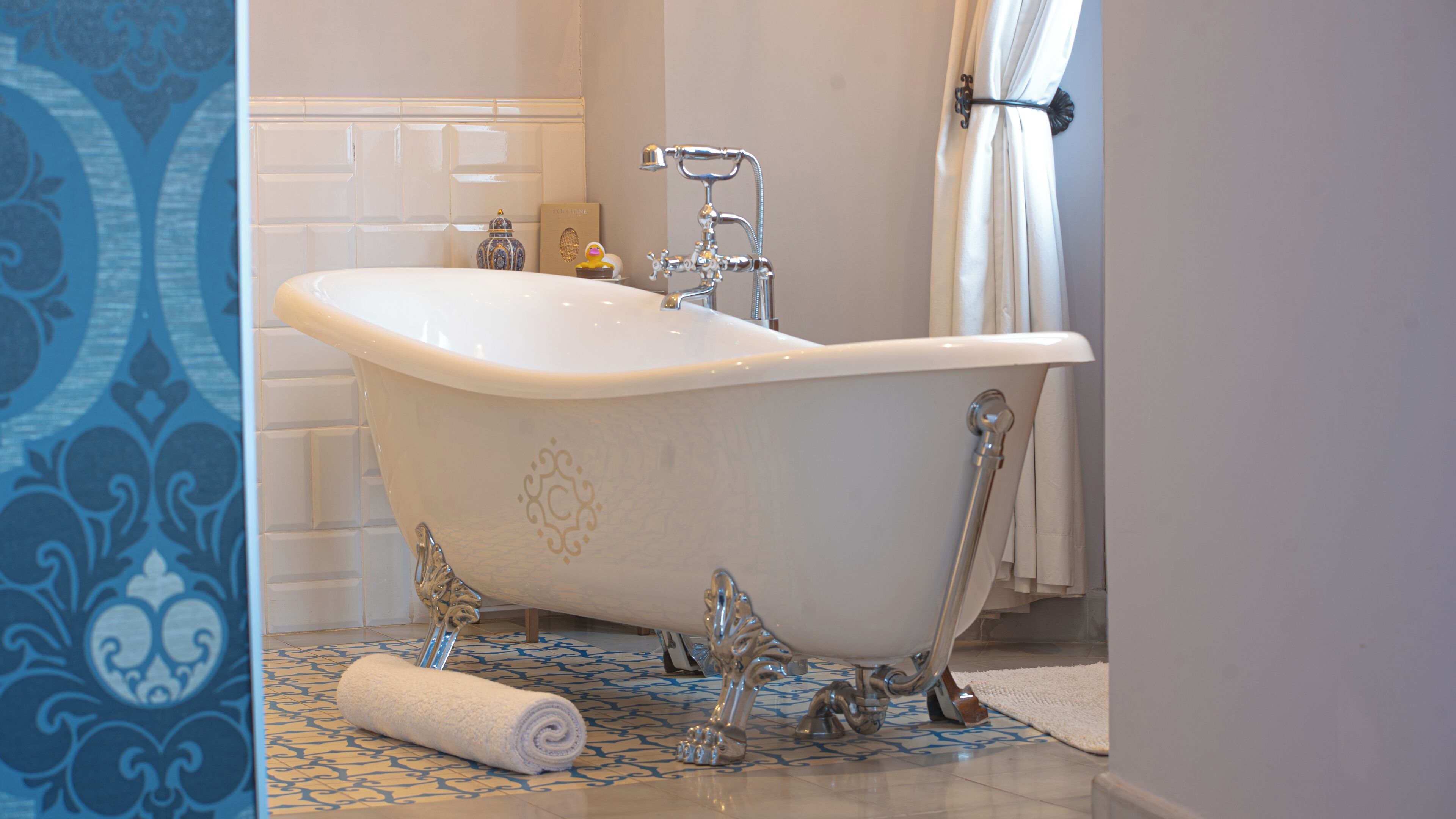 A clawfoot bathtub in a bathroom with a patterned floor and a towel on the floor.