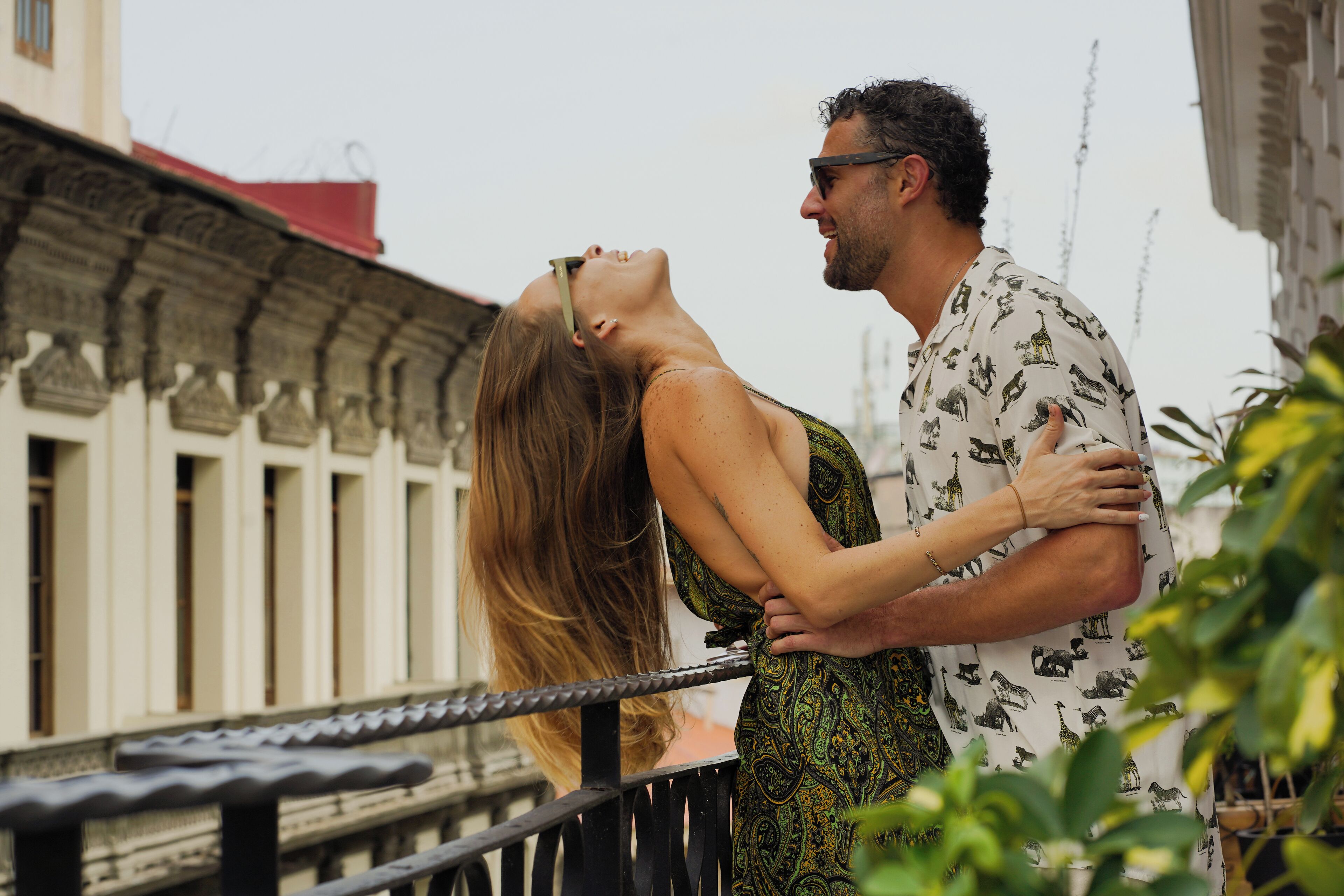 A couple embracing on a balcony with a building in the background.