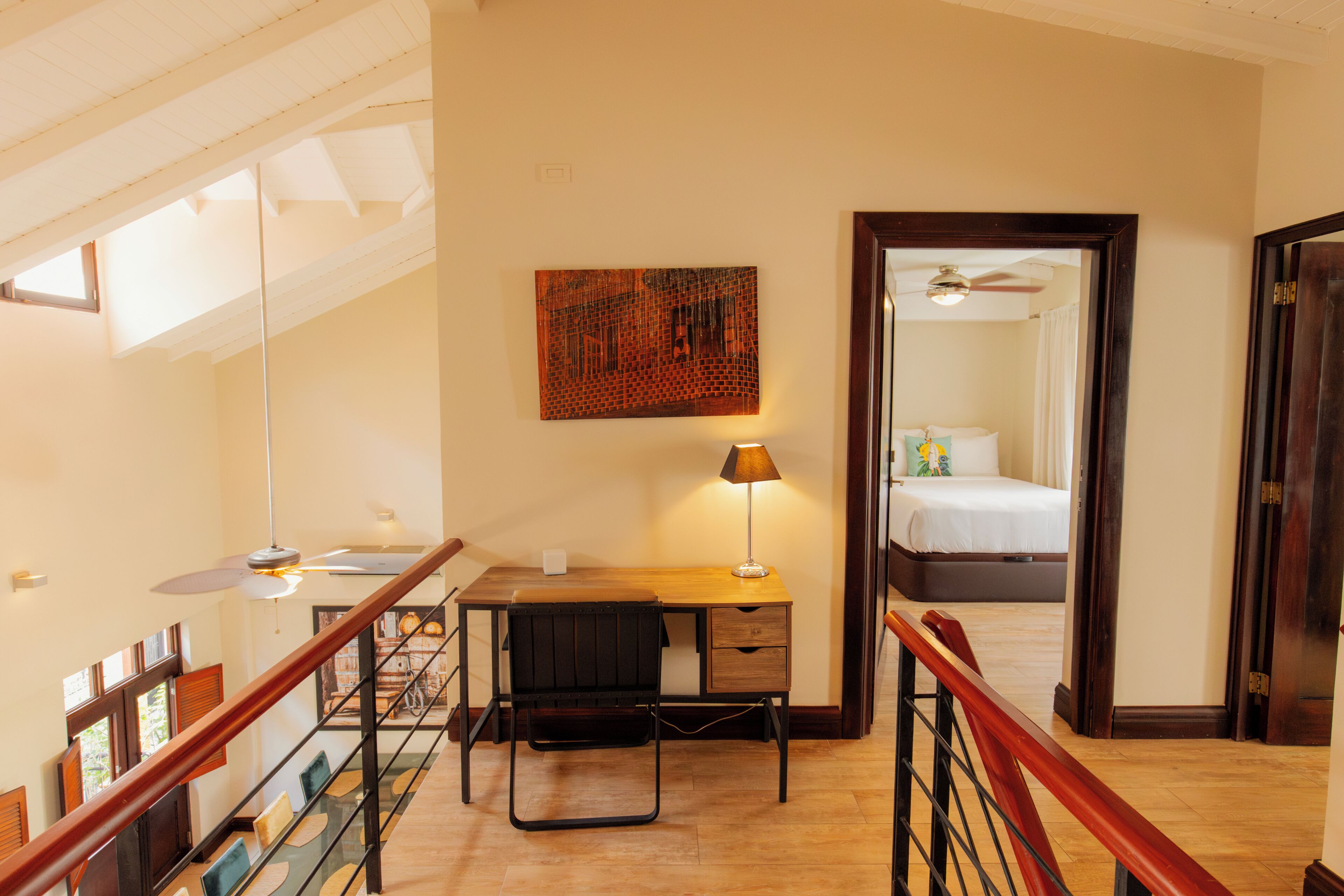 Habitación de hotel con escritorio de madera, una silla, lámpara, cama y vista al cielo a través de una ventana.