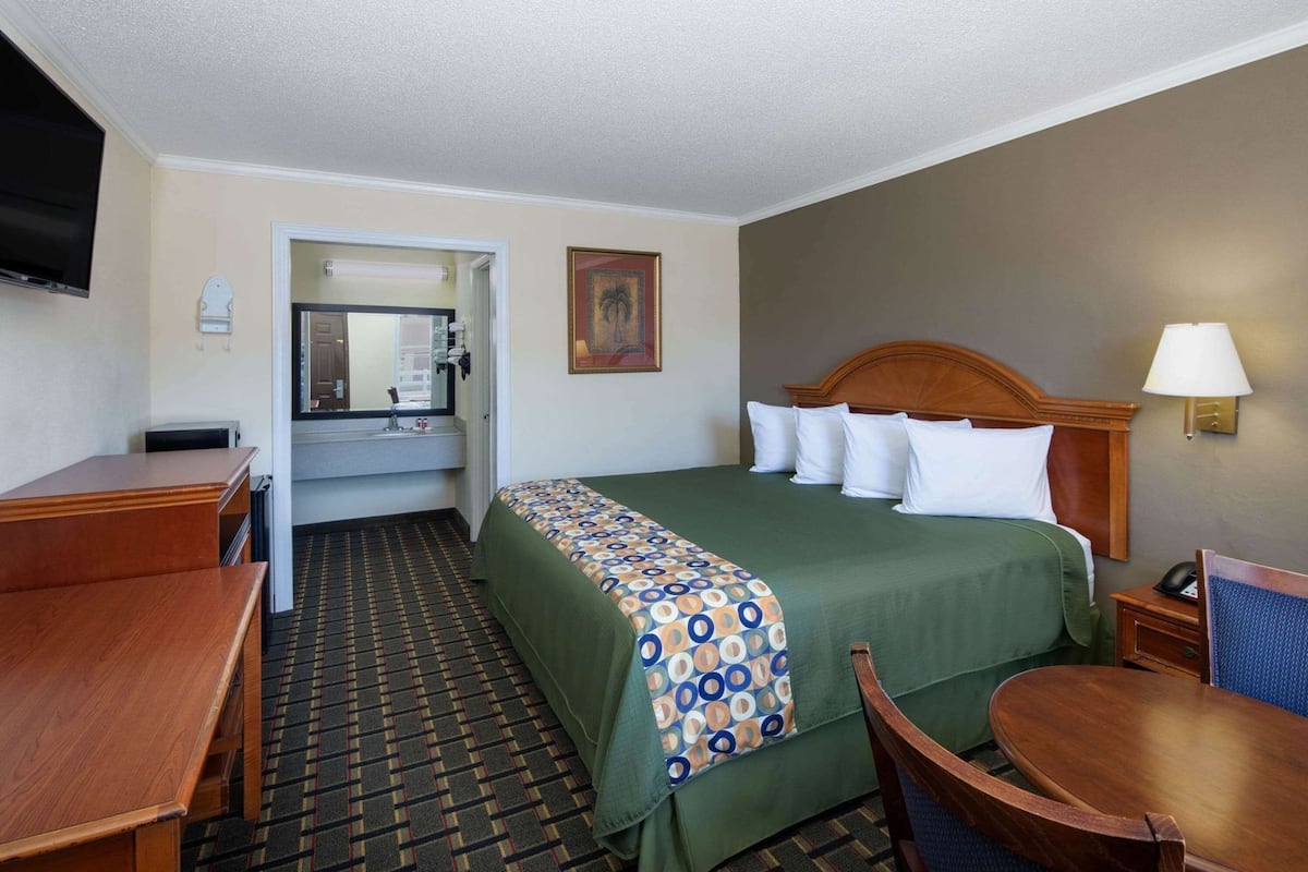 A hotel room with a bed, a desk, a chair, a television, a bathroom, and a painting on the wall.