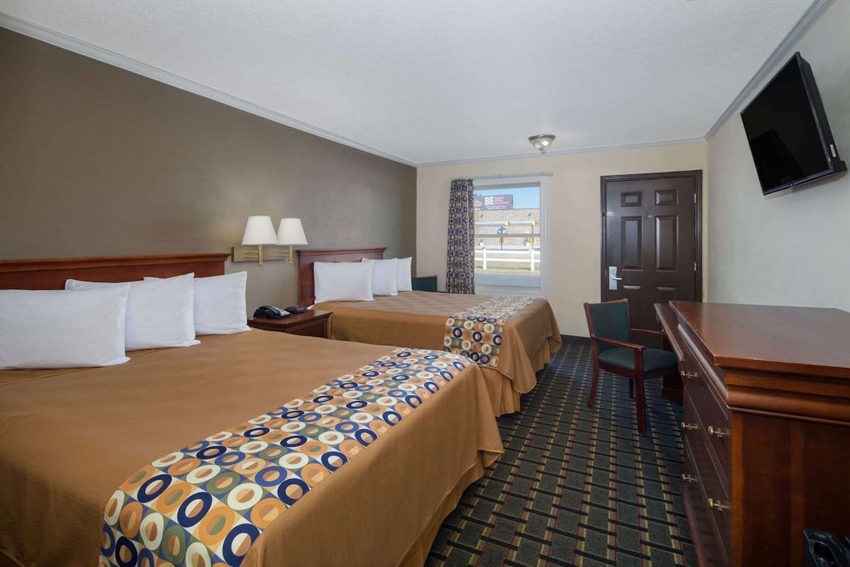 A hotel room with two beds, a desk, a chair, a TV, and a door.
