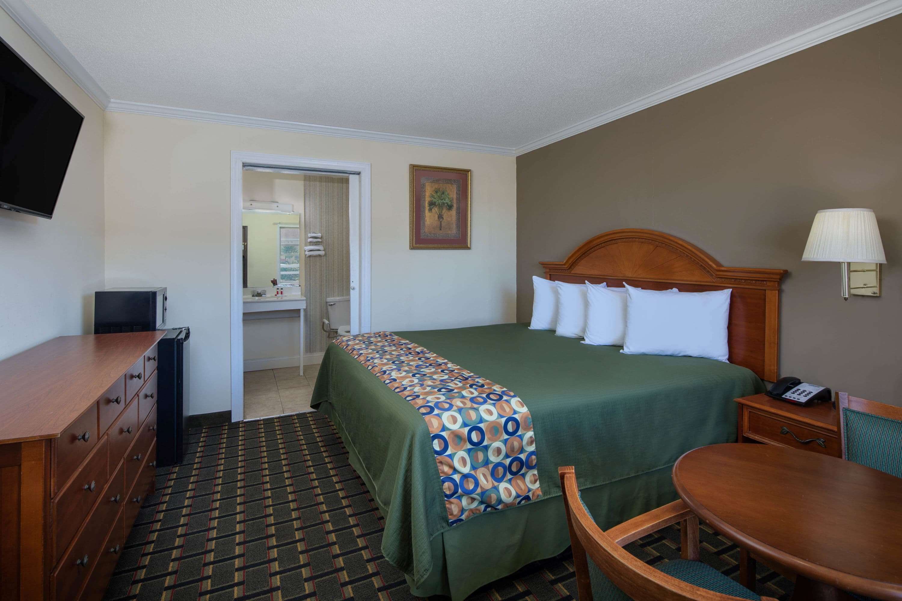 Una habitación de hotel con cama, escritorio, silla, televisor y lámpara.