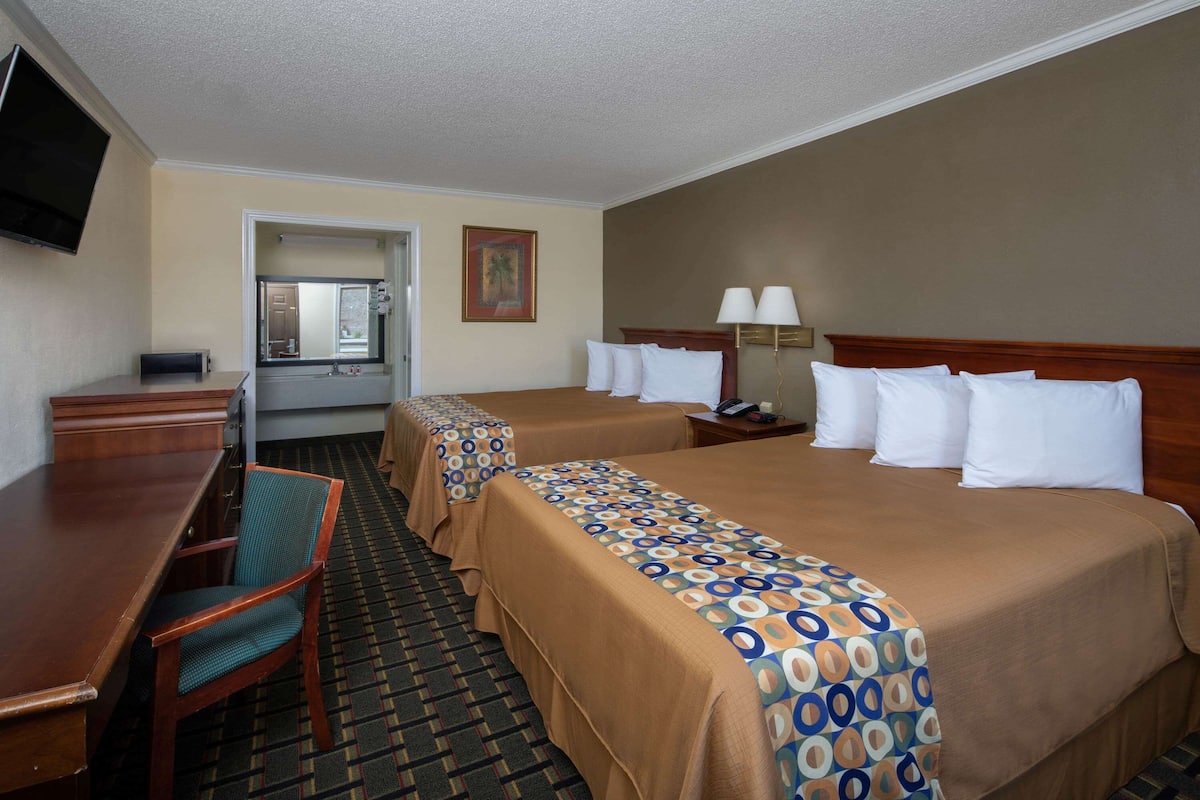 A hotel room with two beds, a desk, a chair, a TV, and a bathroom visible through an open door.