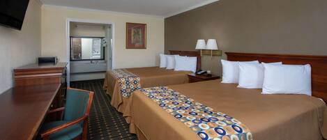 A hotel room with two beds, a desk, a chair, a TV, and a bathroom visible through an open door.