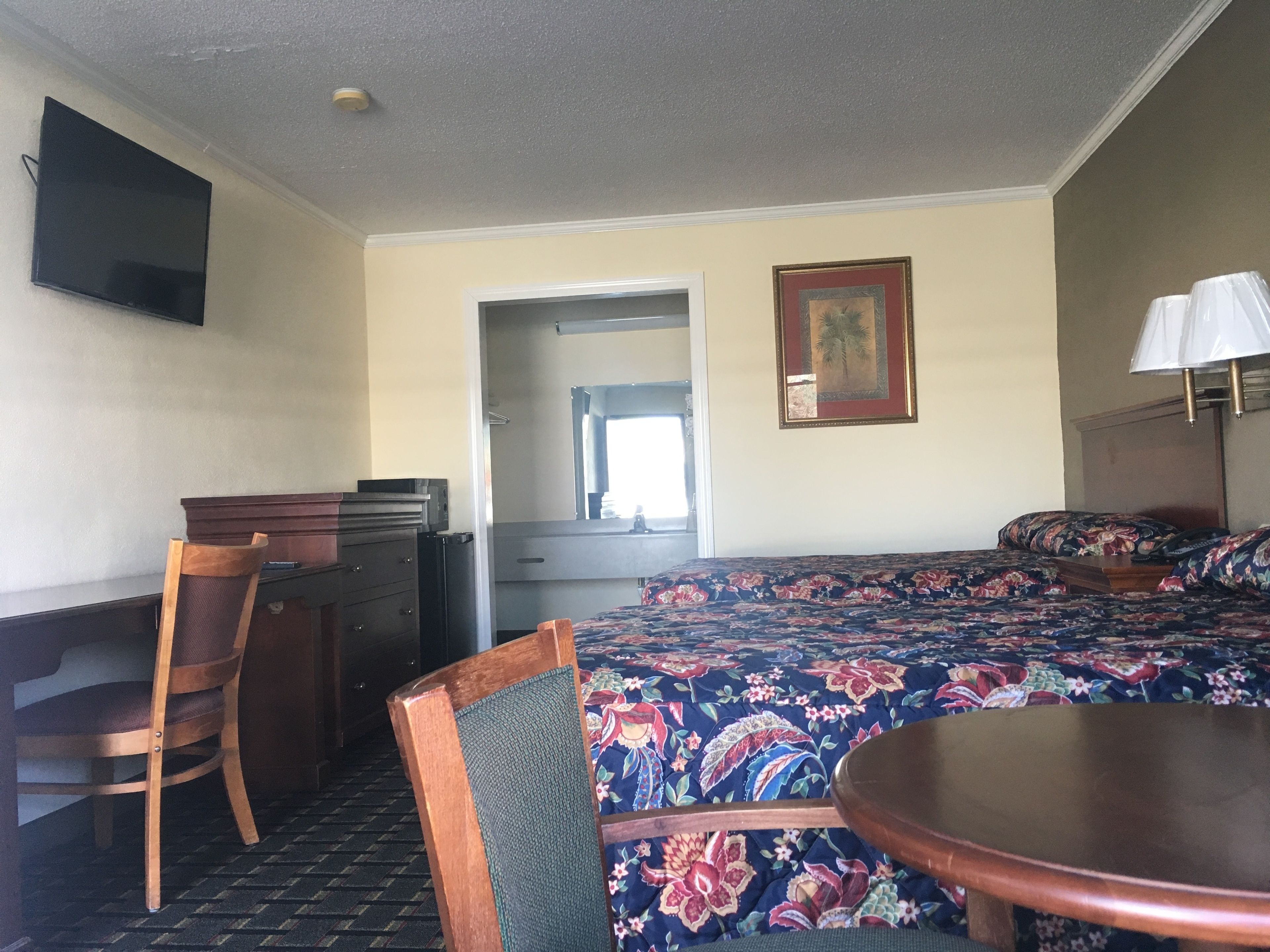 A hotel room with a bed, a desk, a chair, a television, and a painting.
