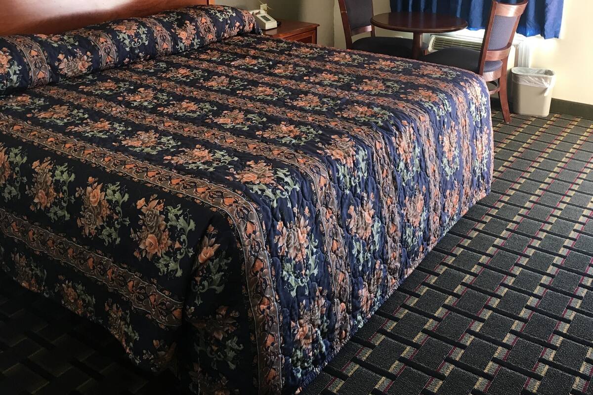 A hotel room with a large bed, a small table, a chair, a lamp, and a window with curtains.