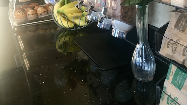 Um balcão de café da manhã com pães, frutas e um vaso de flores.