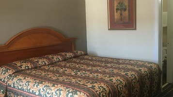 A bedroom with a wooden headboard, a patterned bedspread, a framed picture on the wall, and a checkered floor.