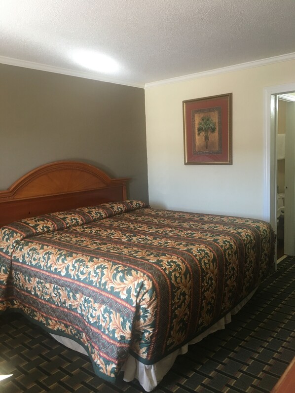 A bedroom with a wooden headboard, a patterned bedspread, a framed picture on the wall, and a checkered floor.
