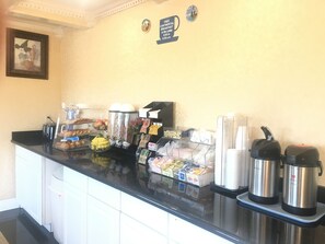 A breakfast bar with various food items, coffee machines, and a sign indicating free continental breakfast.