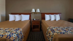 Quarto de hotel com duas camas, uma mesa de cabeceira e duas luminárias na parede.