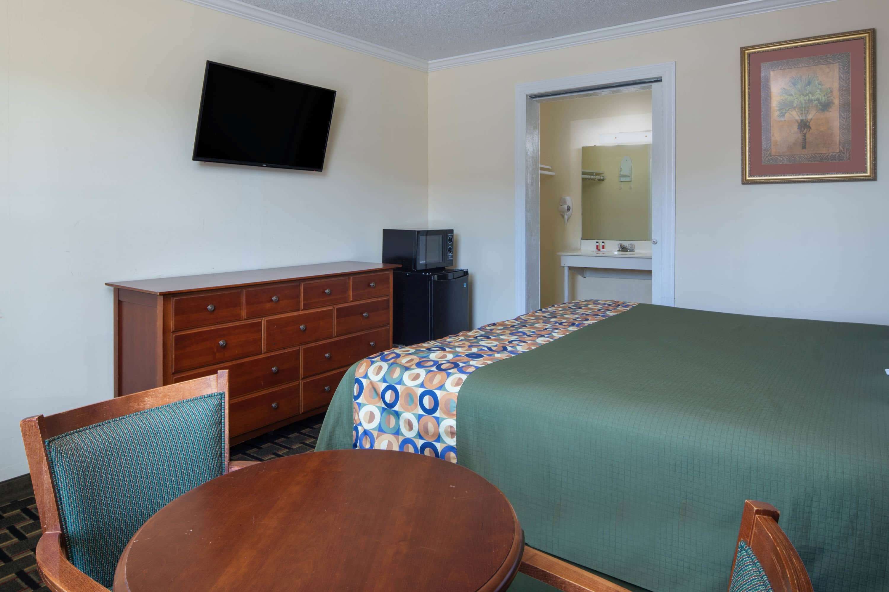 A hotel room with a bed, a TV mounted on the wall, a dresser, a microwave, and a small table with chairs.