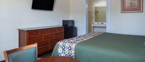 A hotel room with a bed, a TV mounted on the wall, a dresser, a microwave, and a small table with chairs.