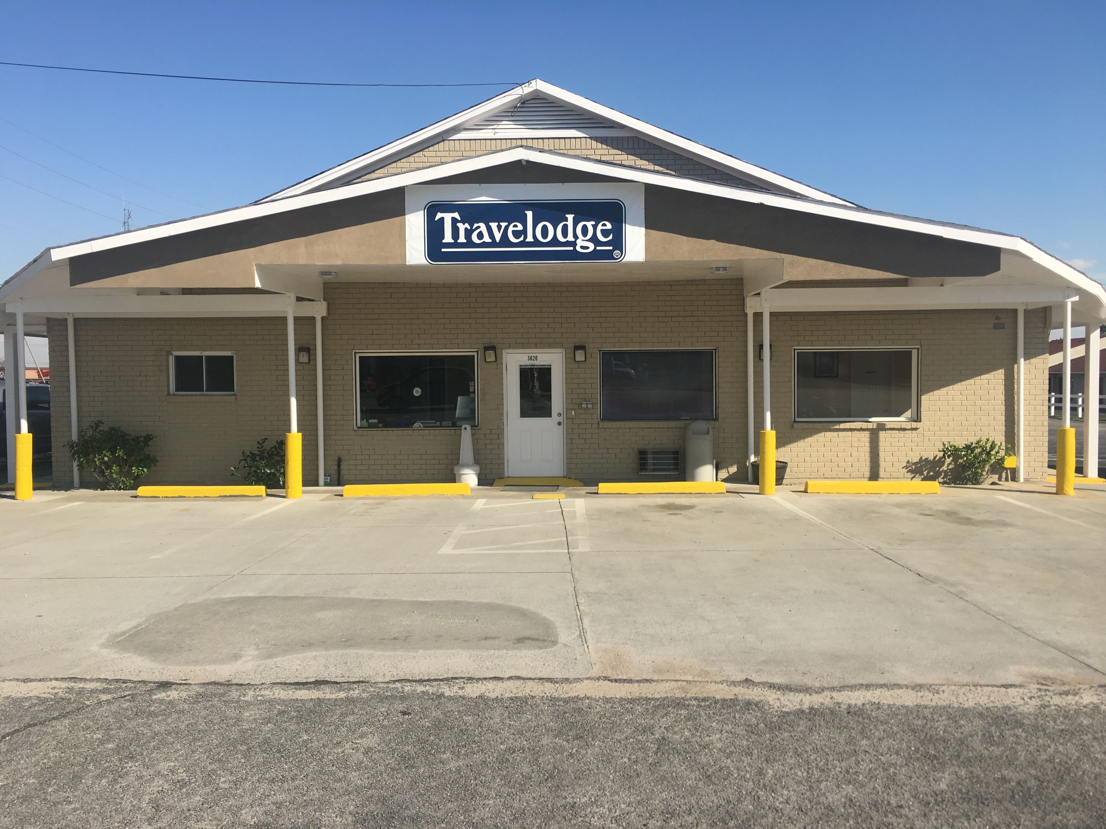 A Travelodge hotel with a simple facade, a prominent sign, and a parking lot in front.