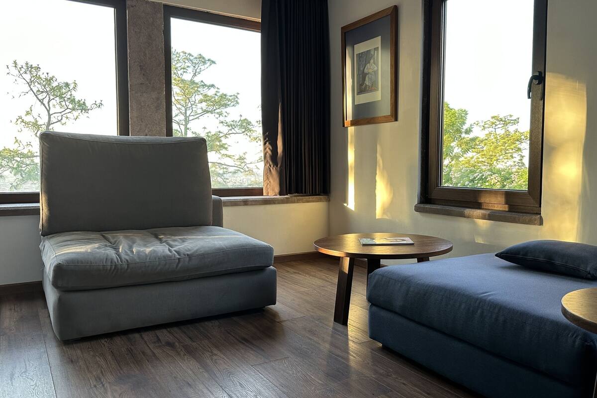 Ein Raum mit grauem Sofa, blauem Sofa, einem kleinen runden Tisch und einem gerahmten Bild an der Wand.