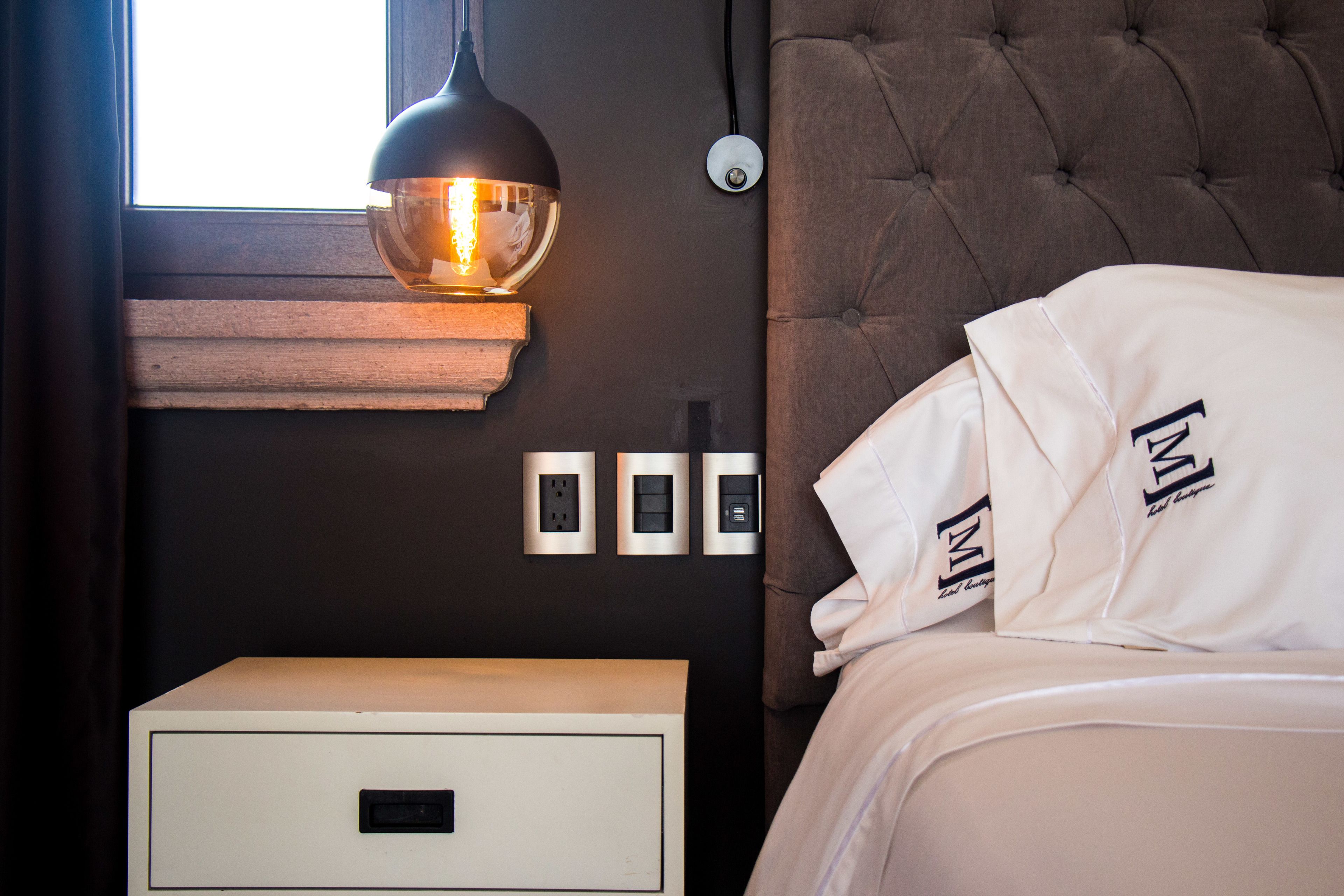 A bedroom with a tufted headboard, a bedside table with a lamp, and a nightstand with a drawer.