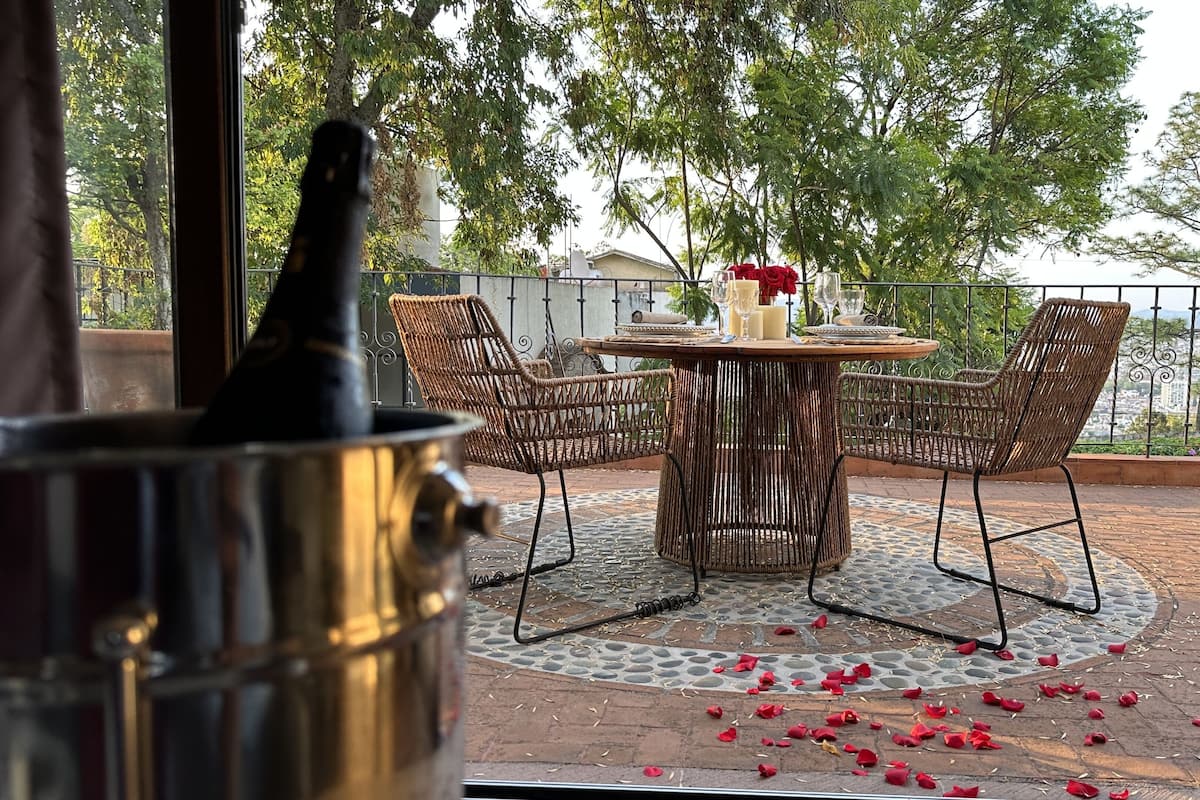 Eine Terrasse im Freien mit Korbstühlen, einem runden Tisch, einem Metalltopf und verstreuten Rosenblüten.