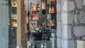 Interior de restaurante com área de bar, paredes de pedra e mesa de jantar de madeira.