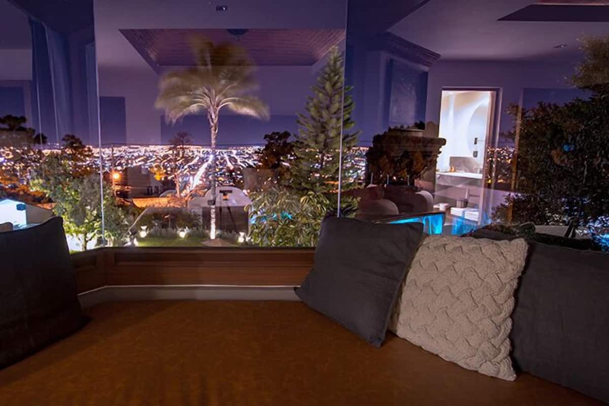 Ein Zimmer mit großem Fenster und Blick auf eine beleuchtete Stadt bei Nacht.
