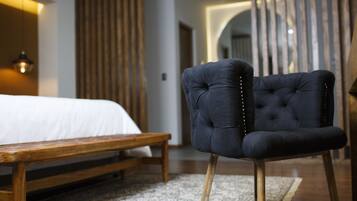 Quarto com uma cama, um banco de madeira e uma poltrona escura estofada com pés de madeira.
