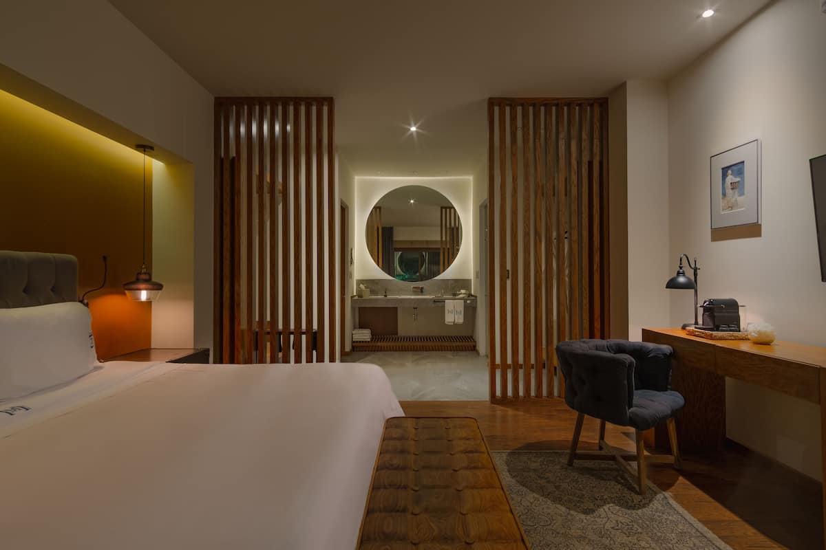 Ein Hotelzimmer mit Bett, Schreibtisch, Stuhl und einem durch eine Holzabtrennung sichtbaren Badezimmer.