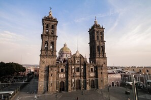 A historic cathedral with two prominent towers and a central dome, surrounded by a plaza with a few people and vehicles. - Casa Rosa Gran Hotel Boutique (Puebla)