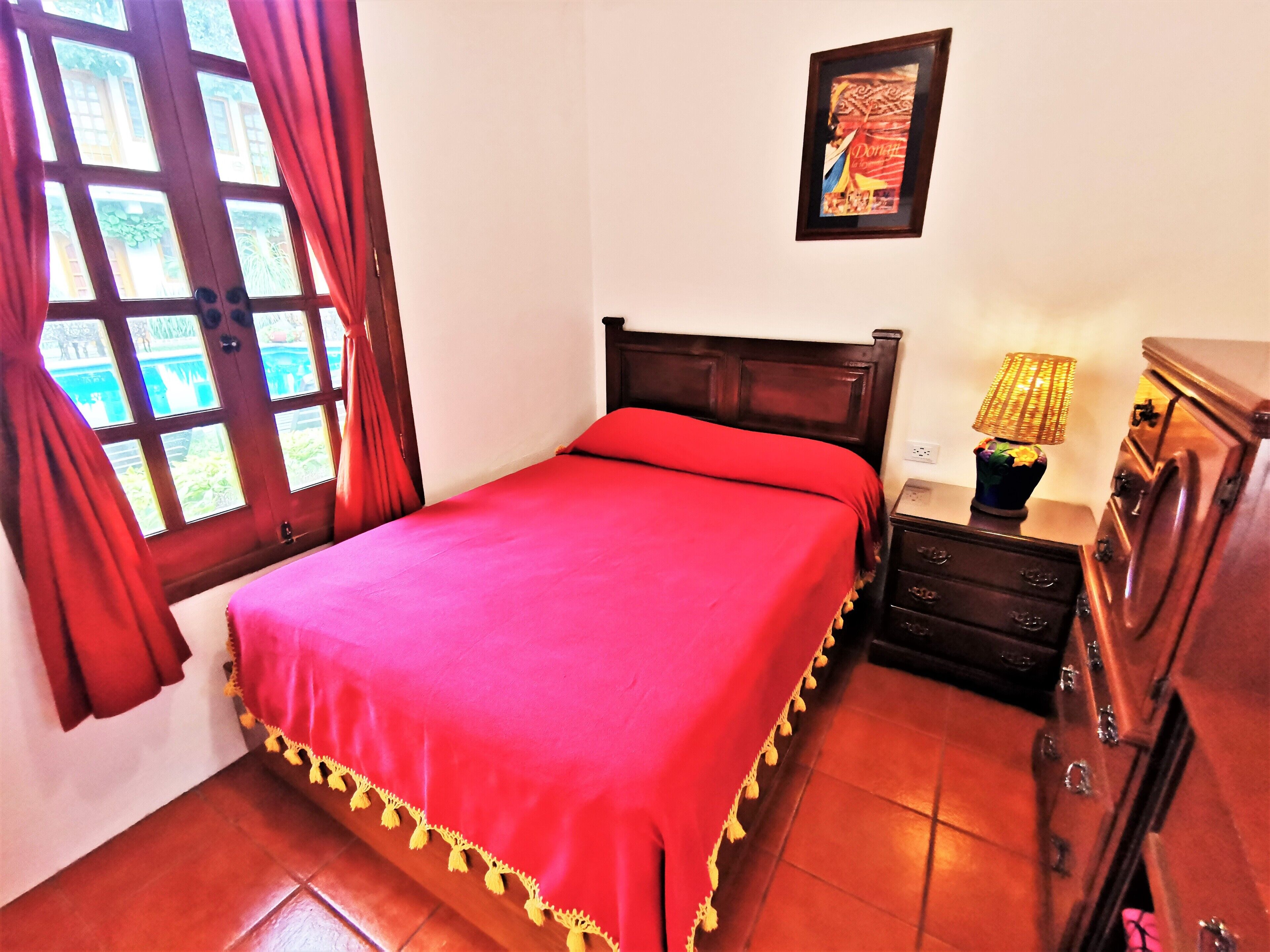 Quarto com cama grande, mesa de cabeceira, penteadeira e janela com cortinas.