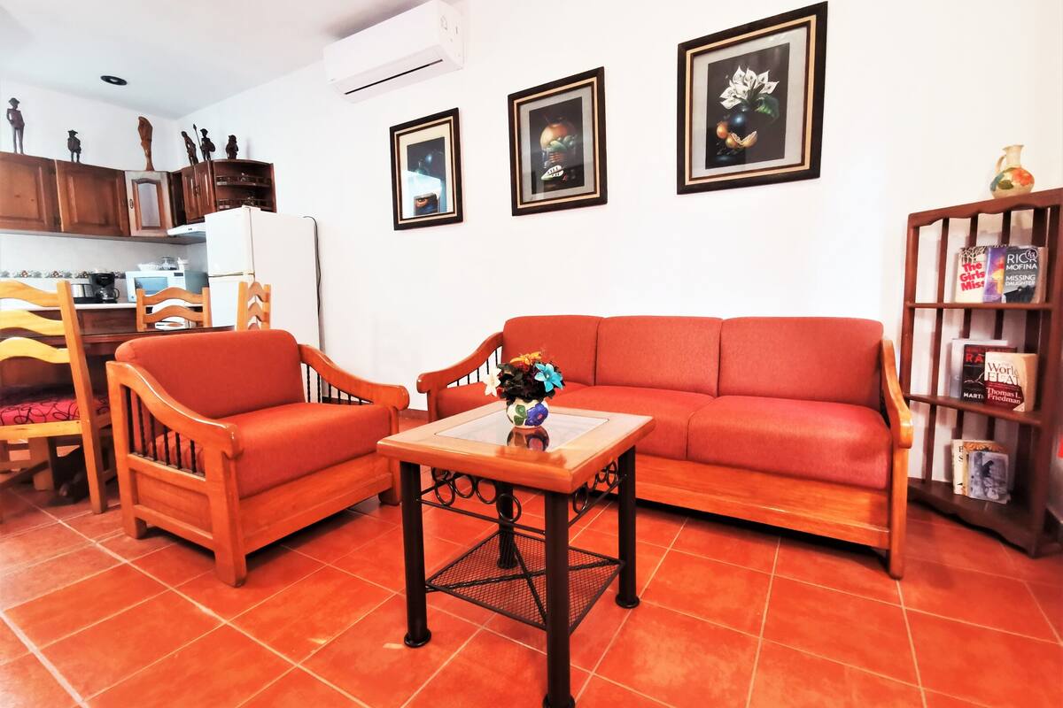 Una sala de estar con un sofá rojo, dos sillas de madera, una mesa de centro y una estantería.
