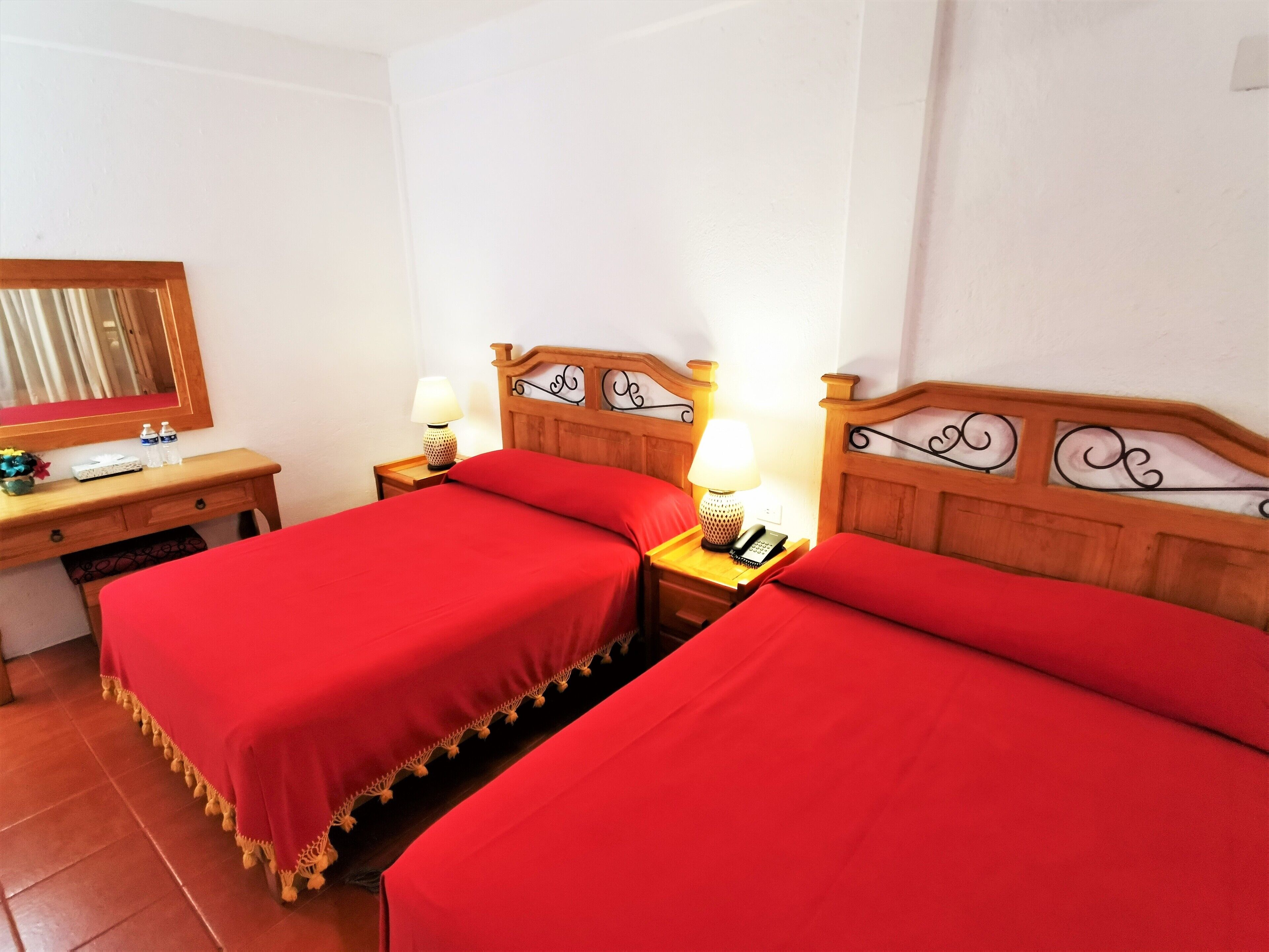 Ein Hotelzimmer mit zwei Einzelbetten, Holz-Kopfteilen, Nachttischen mit Lampen, einem Holztisch und einem Spiegel.