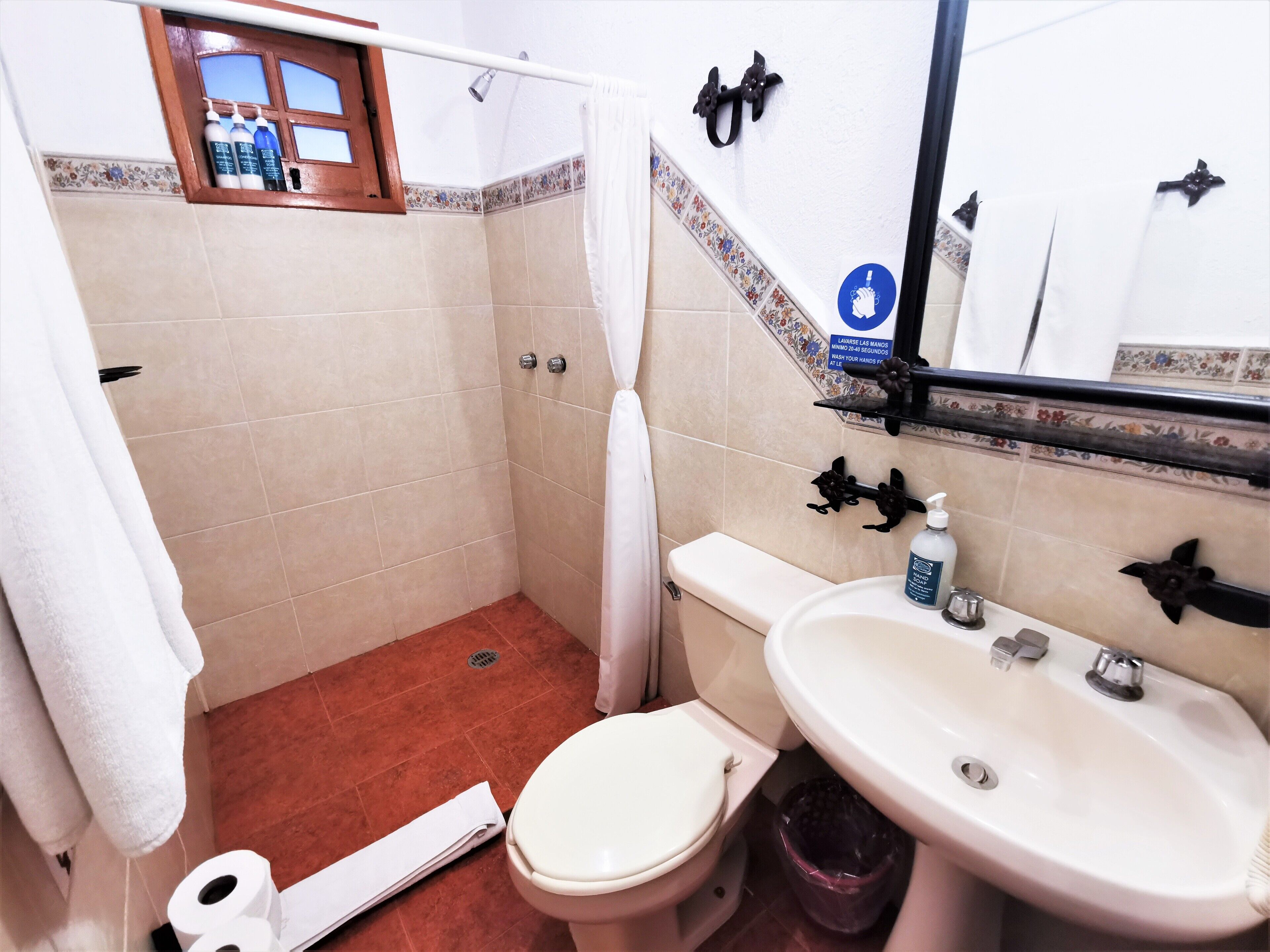 Une salle de bain comprenant des toilettes, un lavabo, une douche et une fenêtre sur le rebord de laquelle sont posées des bouteilles.