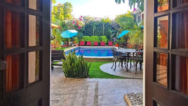 Un espace piscine extérieur avec un chemin en pierre, entouré de verdure et agrémenté de chaises rouges.