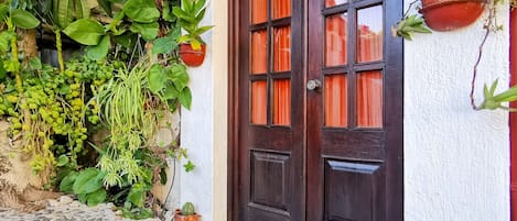 A stone-paved entrance with a dark wooden door and a white wall.