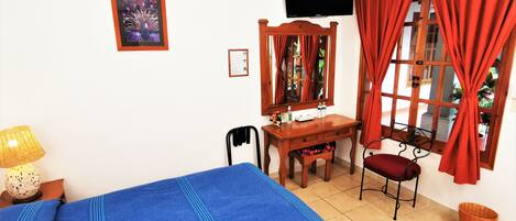 A room with a bed, a desk, a chair, a television, and a window with curtains.