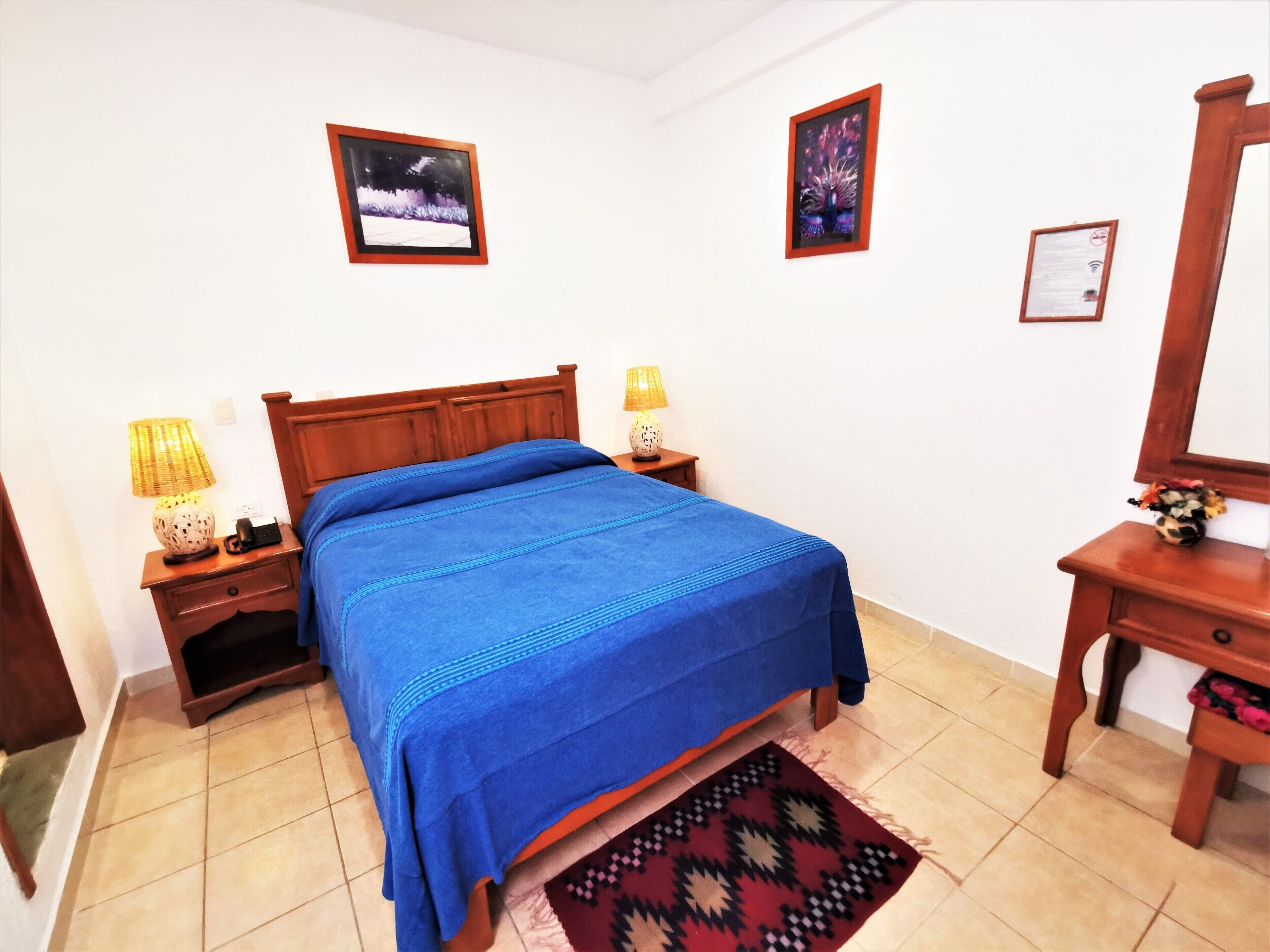 Un dormitorio con una cama de madera, dos mesitas de noche con lámparas, un atril y un cuadro enmarcado en la pared.