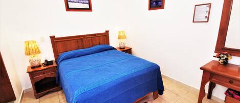 Un dormitorio con una cama de madera, dos mesitas de noche con lámparas, un atril y un cuadro enmarcado en la pared.